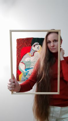 a woman with long hair holding up an art piece in front of her face and looking at the camera