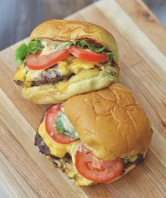 two hamburgers with cheese, tomatoes and lettuce on a wooden cutting board