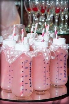 four baby bottles with straws in them on a glass table next to wine glasses