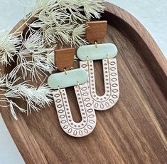 two wooden earrings with white and green designs on top of a wooden tray next to pine branches