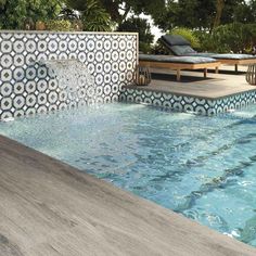 an outdoor swimming pool with water running from the side and lounges in the background