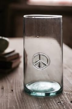 a glass with a peace sign on it sitting on a wooden table next to stacks of books