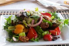 a salad with meat and vegetables on a plate next to a fork, knife and napkin