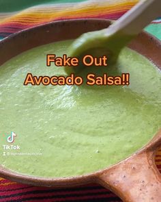 a bowl filled with green soup sitting on top of a colorful table cloth next to a wooden spoon