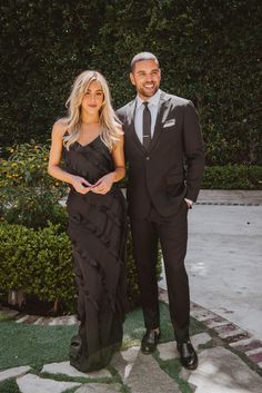 a man and woman standing next to each other in front of some bushes wearing formal attire