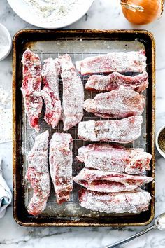 raw meat on a baking sheet covered in powdered sugar and seasoning next to other ingredients