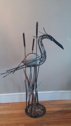 a metal bird sculpture sitting on top of a wooden floor next to a white wall