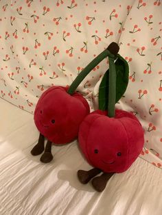 two stuffed cherries sitting on top of a bed next to each other with leaves