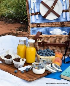 an open picnic basket with fruit, juice and other food on the table next to it