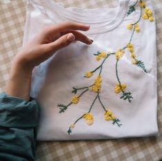 someone is stitching yellow flowers on a white t - shirt with green trimmings