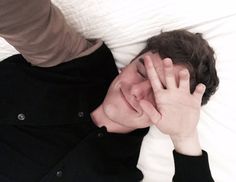 a man laying in bed with his hands on his face