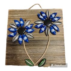 two blue and silver flowers are on a wooden board with some string attached to it