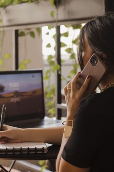 a woman sitting at a desk talking on her cell phone and writing in a notebook