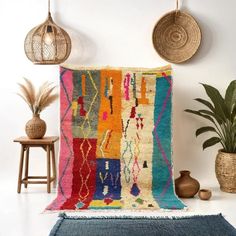 a multicolored rug is displayed on the wall next to two potted plants