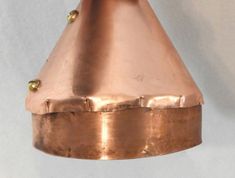 a copper colored light hanging from a ceiling fixture with gold studs on the top