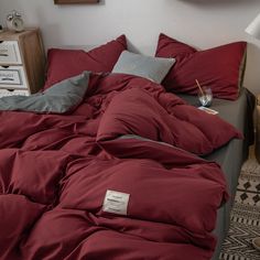 an unmade bed with red sheets and pillows