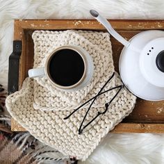 a cup of coffee sitting on top of a wooden tray next to a knitted blanket