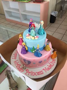 there is a birthday cake with princess figures on the top and bottom tier, in a box