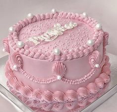 a pink birthday cake with pearls on the top and name written in white frosting