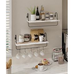 two white shelves with cups and coffee mugs on them next to a counter in a kitchen