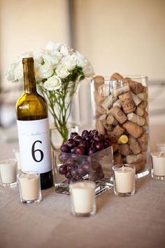 a table topped with wine bottles and glasses filled with white flowers next to candle holders