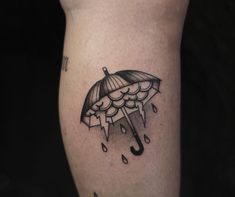 a black and white tattoo of an umbrella with rain drops on the side of his leg