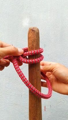 two hands are holding a rope that is attached to a wooden pole with one hand