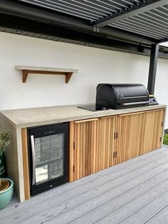 an outdoor kitchen with a grill and microwave on the outside deck, next to a potted plant