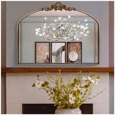 a vase filled with flowers sitting next to a mirror on top of a fireplace mantle