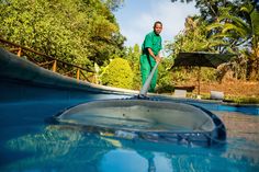 a man in green jumpsuits is cleaning the pool with a mop and an umbrella