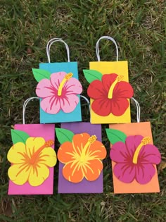 four small bags with flowers on them are sitting in the grass and one has been made out of paper