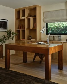 a wooden desk sitting in front of a window next to a potted plant on top of a hard wood floor