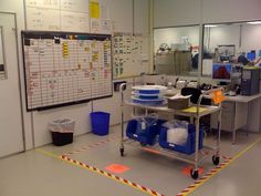 a room with several tables and bins on the floor in front of a whiteboard