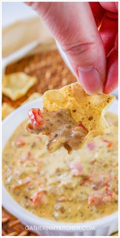 a hand holding a tortilla chip over a bowl of quesadilla soup