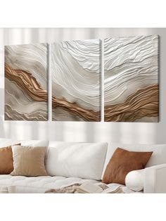 three abstract paintings on the wall in a living room with white couches and pillows