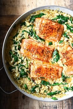 salmon and spinach on rice in a skillet with a wooden table behind it