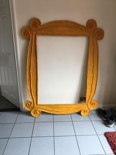 a yellow framed mirror sitting on top of a white tiled floor next to a door