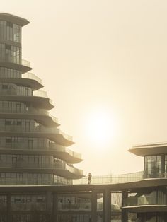 the sun is setting behind a tall building with balconies on each floor and two people standing on top