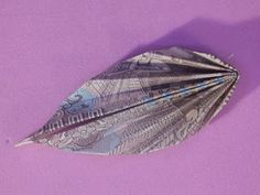 a feather is laying on top of a purple surface and it looks like an origami bird