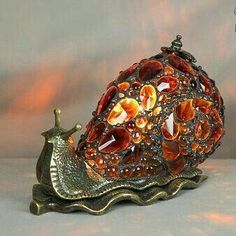 a snail figurine sitting on top of a metal base with red and yellow glass beads