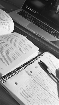 an open book sitting on top of a desk next to a laptop computer and pen