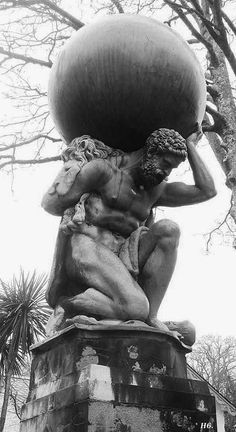 black and white photograph of a statue holding a large object on top of it's head