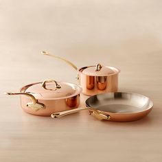 three copper pots and pans on a table with one being used as a cooking utensil