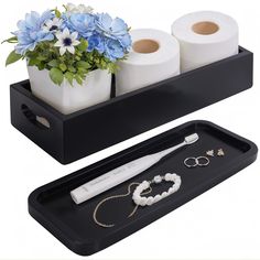 two black trays with white and blue flowers in them, one holding three rolls of toilet paper