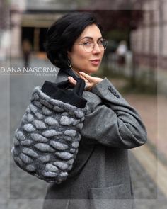 a woman in glasses is carrying a gray handbag on her shoulder and looking off to the side