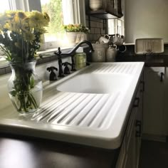 a white sink sitting under a window next to a vase with yellow flowers in it