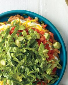 a blue bowl filled with lettuce, tomatoes and other vegetables on top of a white table