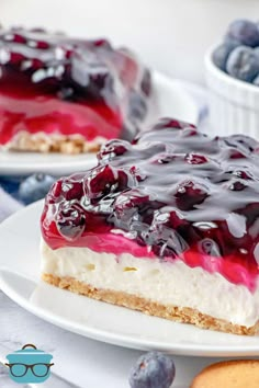 two slices of cheesecake with blueberry sauce on top and glasses in the background