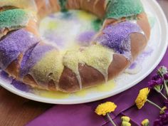 a bundt cake with purple, yellow and green icing on a plate next to flowers