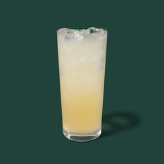 a tall glass filled with yellow liquid on top of a green table next to a black background